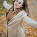 Woman in Beige Long Sleeve Coat Standing on Brown Leaves