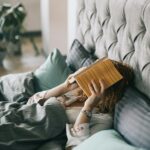 Woman Covering Face With Book on Bed
