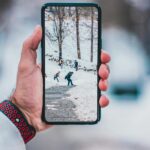 Hand holding smartphone displaying a winter scene with people walking on snow-covered path.