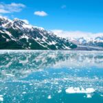 A breathtaking view of Alaskan glaciers reflecting on tranquil icy waters under a clear blue sky.