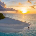 A couple enjoys a serene sunset on a pristine Maldives beach.
