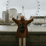 Person with arms raised viewing the London Eye across River Thames in autumn.